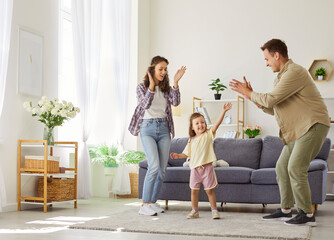 Mother and father with daughter having fun and dance together at home. Parents clap in a bright...