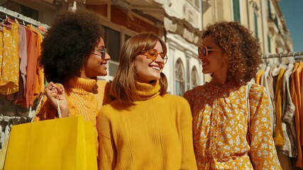 Three Happy Diverse Young Women Friends in Yellow Outfits and Sunglasses Shopping on a Sunny Street Market