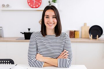 POV screen view of young female having a video call, listening to friend or colleague. Smiling portrait of happy woman sitting on kitchen table working at home