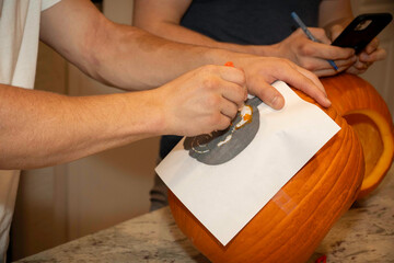 focused homeowner outlining pattern on pumpkin using pencil amidst warm ambient lighting for festive craft