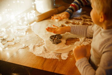 Children making homemade cookies from dough with Christmas cookie cutters on wooden table in warm festive kitchen light, kids baking holiday treats together, cozy family winter activity