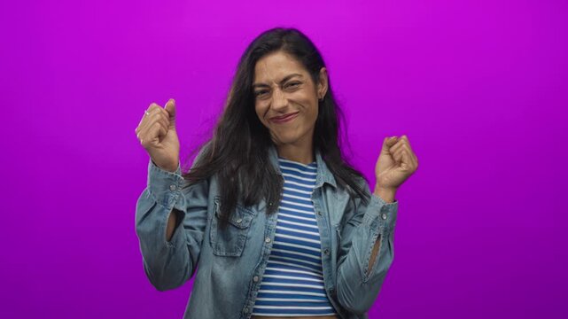 Woman pointing finger at camera showing hand and striped midriff in studio with purple backdrop; invitation confidence.
