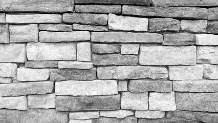 A closeup of a stone wall with rough uneven rectangular blocks stacked in a horizontal pattern showing natural texture detail and a rustic architectural background in grayscale