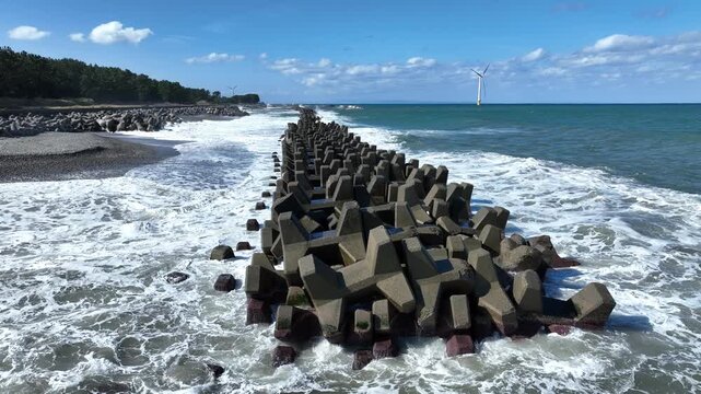 冬が近く風の強い富山湾沿岸の洋上風力発電風車や波のかかる離岸堤などの風景