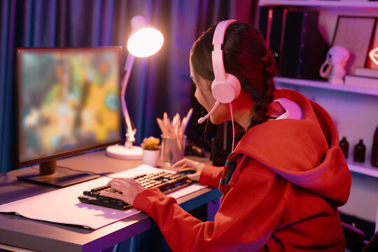 Host channel of young beautiful Asian gaming streamer playing fighting Moba at battle arena game on pc screen with multiplays, wearing pastel headphone at neon digital light modern room. Stratagem. - Powered by Adobe