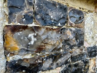 Close view of knapped flint blocks set in limestone, forming the medieval chequerboard masonry of Saint-Martin Church in Saint-Valery-sur-Somme, Picardy, with glossy textures and weathered patina