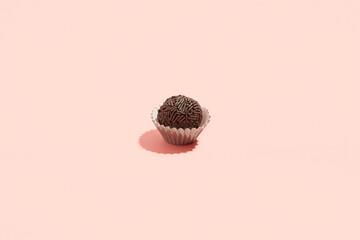 Typical Brazilian sweet brigadeiro. One candy with chocolate sprinkles on a pink background