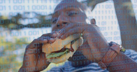 Biting man wearing blue-and-white striped shirt holding two burgers at park, with 0s and 1s overlay