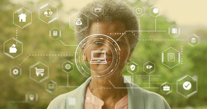 Standing senior woman wearing cardigan and pink blouse in garden, showing HUD laptop and hex icons - Powered by Adobe