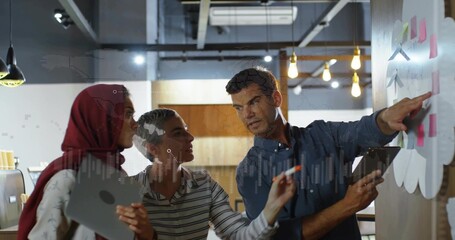 Pointing trio in red hijab and striped top discussing planning wall in office with sticky notes