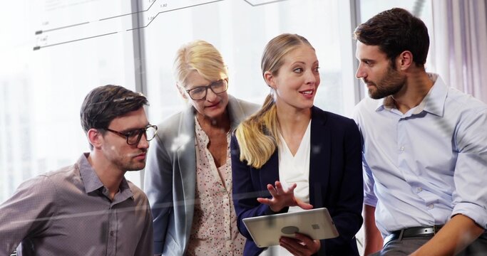 Gesturing presenter and coworkers leaning around tablet by windows, in blazers, reviewing charts - Powered by Adobe