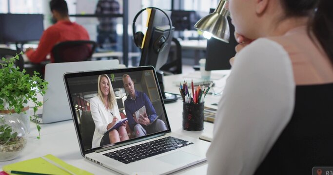 Leaning female worker watching laptop virtual meeting at open-plan office, in white top, copy space - Powered by Adobe