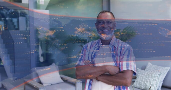 Standing mature man crossing arms facing camera in living room, in plaid shirt, glass reflections