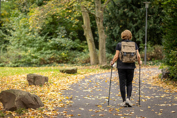 Enjoying a peaceful walk on a leaf-covered path in a forest park during autumn with hiking poles and a backpack