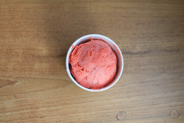 Scoop of strawberry sorbet in paper cup on wooden table. Summer food dessert concept.
