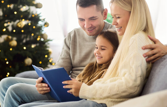 Christmas family reading a book together. In a cozy livingroom, parents and daughter read by the tree, savoring holiday warmth and moments. Concept: festive family time and togetherness.