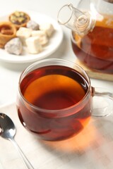 Tasty tea in glass cup and teaspoon on white table, closeup