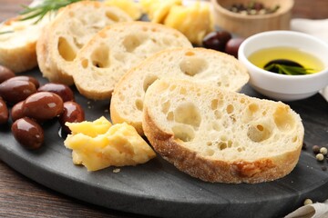 Pieces of fresh ciabatta, oil, olives, cheese and peppercorns on wooden table, closeup
