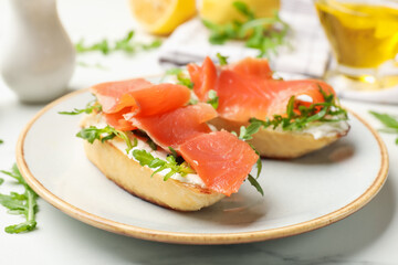 Tasty bruschettas with salmon and arugula served on white marble table, closeup