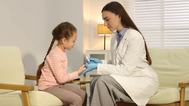 Diabetes. Smiling doctor in medical gloves checking little girl's blood sugar level with lancet pen and glucometer on armchair indoors