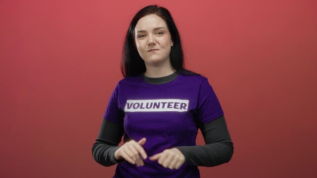Beautiful brunette woman wearing volunteer shirt claps joyfully in front of vibrant red background radiating happiness and engagement