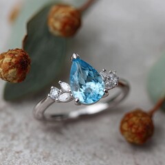 Blue teardrop gem ring framed by dried foliage on textured surface