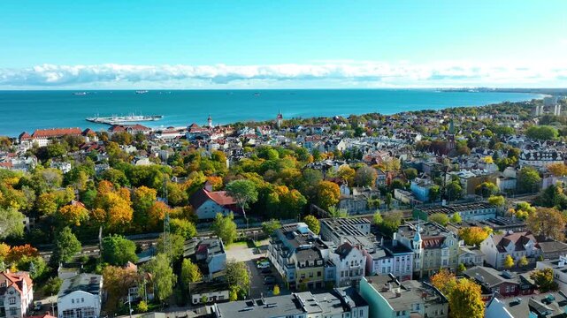 Drone view of Sopot showing historic city center, colorful trees, and Baltic Sea horizon