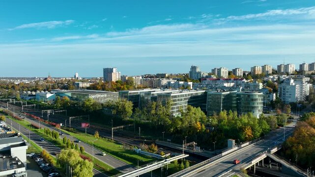 Wide aerial drone shot of modern glass office buildings and the adjacent rail and road infrastructure, set against a city skyline - PPNT Gdynia