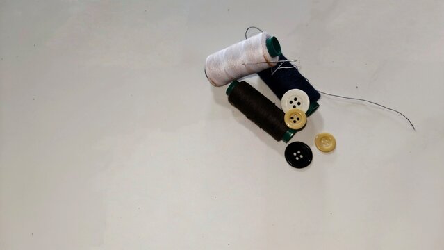 Spools of thread and assorted buttons on a white background, symbolizing sewing and craftsmanship. This minimalist photo is perfect for fashion blogs, tailoring service promotions, DIY tutorials