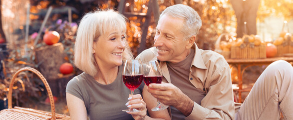 A happy couple enjoys a moment together outdoors in autumn, holding glasses of red wine. The warm golden light creates a charming atmosphere filled with joy and connection.