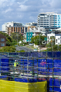 Tradies behind safety mesh and scaffold of new building construction site.