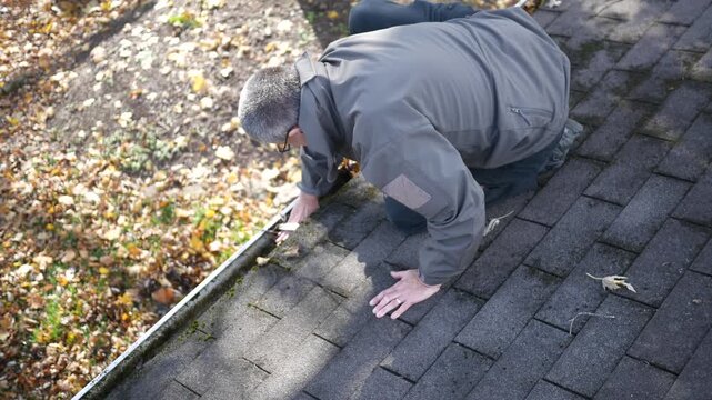 Older Man Cleans Gutters on Roof of House.