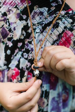 Young child wearing a woven necklace while holding a shell pendant.