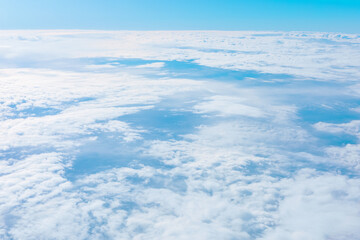 Aerial view reveals a vast sea of clouds stretching endlessly, textured in soft whites and blues. Above sky transitions from deep to pale blue, evoking serenity and grandeur of high-altitude flight