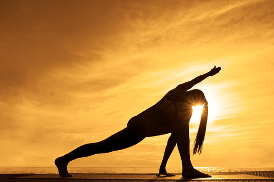 Parivrtta Parsvakonasana Revolved Side Angle Pose Sporty latin hispanic woman doing posture outdoor full length profile side view on sea lake river park background Evening Sunset Sunrays sunbeams beam