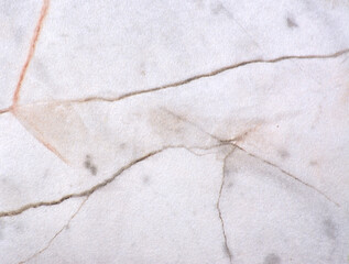 Gray marble, polished natural stone surface with deep black and orange cracks throughout the material, close-up.