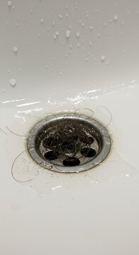 Clogged bathroom sink drain with wet hair and water drops