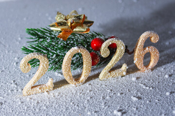 Festive 2026 New Year numbers in sparkling gold glitter with pine branch on white snow background....