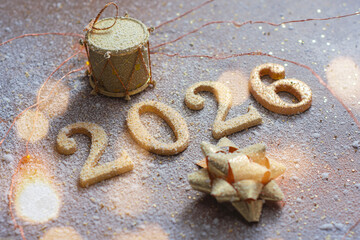 Golden 2026 numbers with decorative bow and holiday drum covered with snow on a festive background. Winter Christmas and New Year celebration concept for greeting cards and holiday design.