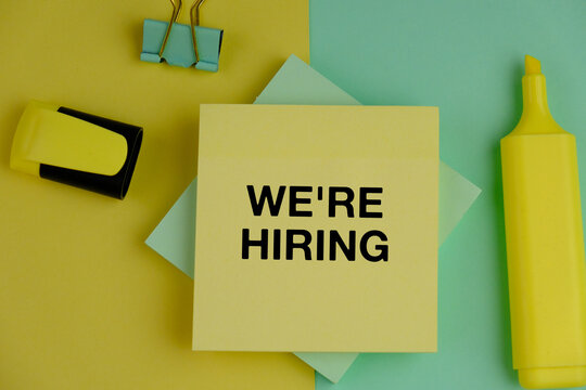 we are hiring text on white paper as a hiring and job searching concept. alarm clock, books and frame. 