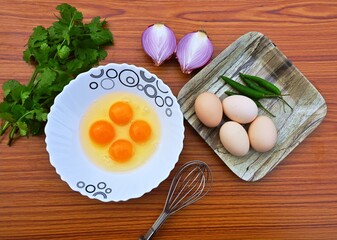 eggs recipe, Cooking ingredients for egg omlette, eggs, onion, green chilli, coriander leaves with whisk on a table. Top view. Healthy breakfast concept.