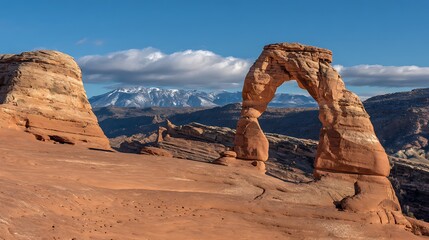 Delicate arch in arches national park, utah, usa, under a clear blue sky with scattered clouds and snowcapped mountains in the background, a natural sandstone wonder