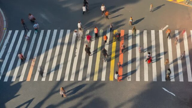 Vista a&eacute;rea de un cruce peatonal con muchas personas caminando sobre rayas blancas y de colores.