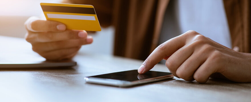 A person holds a credit card in one hand and touches a smartphone screen with the other hand at a table in a cafe. The scene shows a casual atmosphere for making payments.