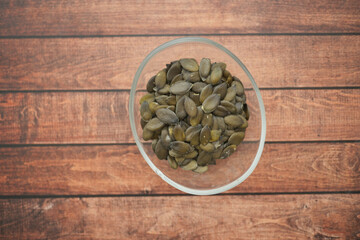 Healthy pumpkin seeds in a glass bowl on wooden table