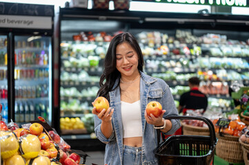 Asian woman standing holding a shopping basket looking or buying apples at fruit zone in supermarket