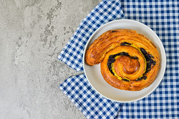 Top view of one raisin roll on white plate. close up. napkin. cement background. High angle, above, flat lay. copy space, empty, free, negative, text, design.