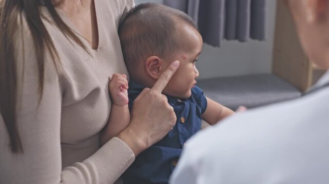 Asian female doctor checking infant with red rash on face, showing allergy or skin irritation symptoms during medical examination in premium clinic or private hospital