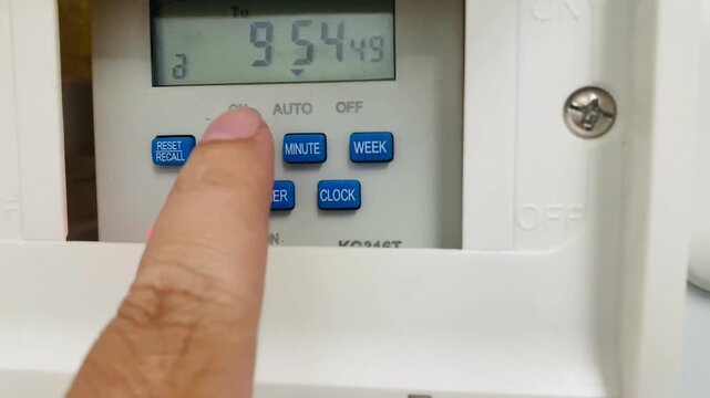 finger pressing a button on a white digital programmable timer