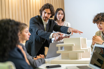 Architects engineers collaborating on building design project in modern office, diverse team of professionals female muslim architect and male engineers discussing architectural model of structure